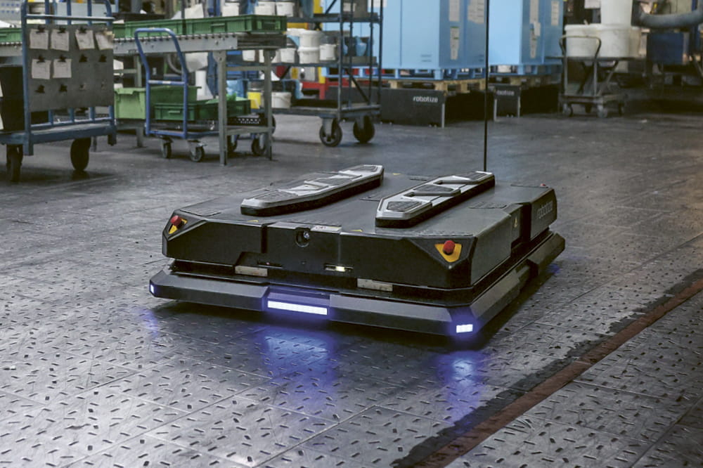 Ein schwarzer quadratischer Roboter GoPalfährt durch eine Lagerhalle